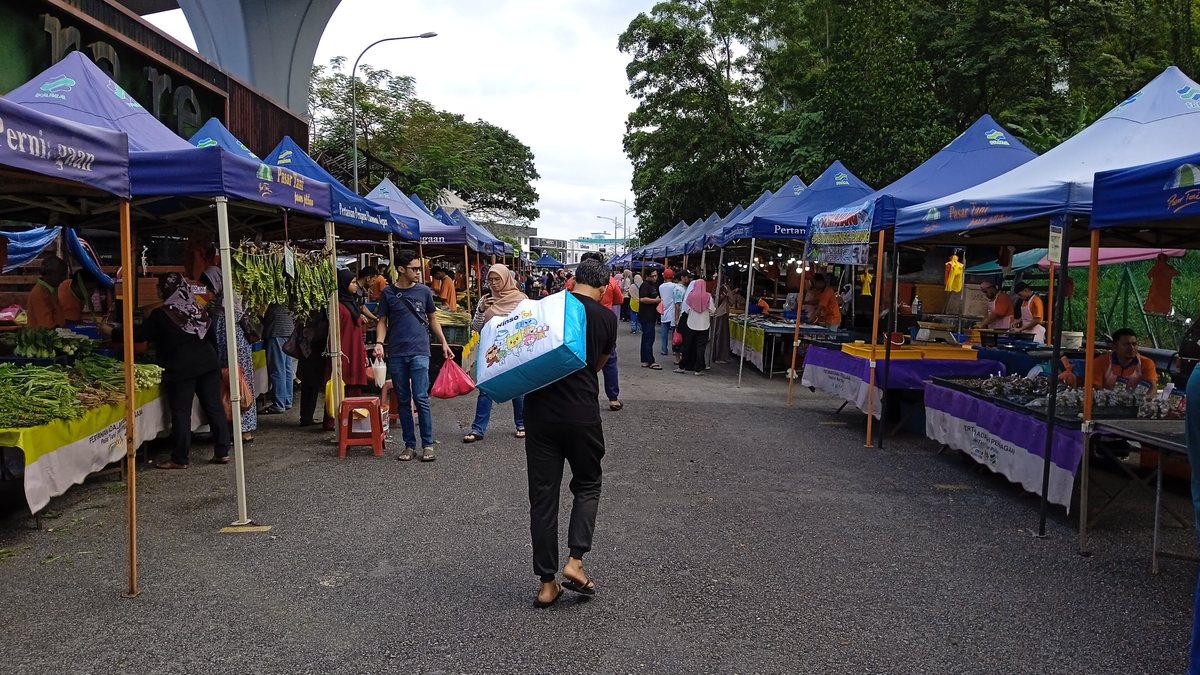 Farmers' market stalls under blue tents with shoppers